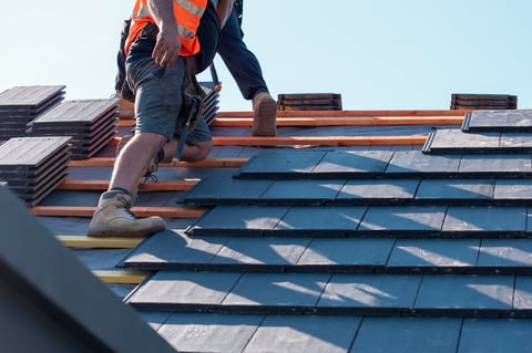 Builder carefully places roof tiles on a sloped surface
