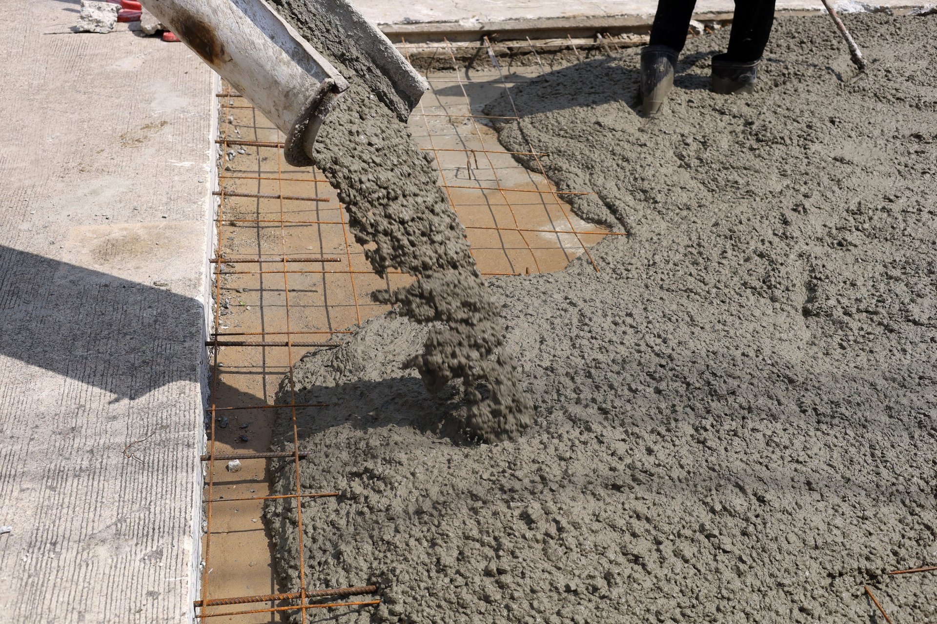 Wet cement pouring from a mixer truck chute onto a steel wire mesh for road